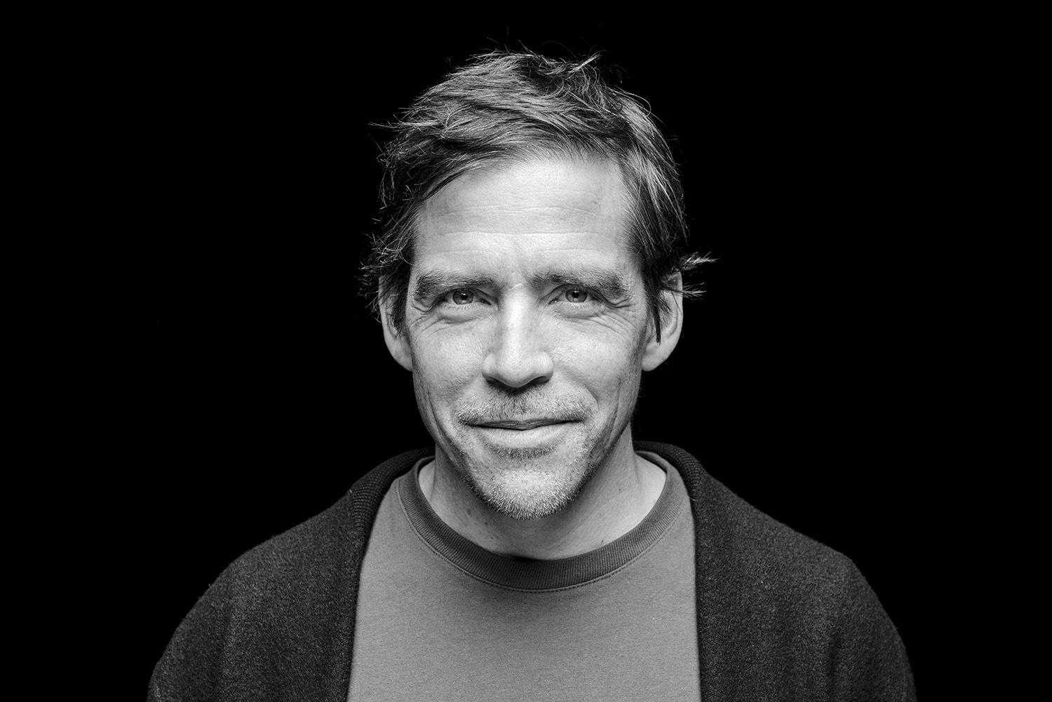 Alexander Bartels, fotografiert in schwarzweiss vor dunklem Hintergrund.